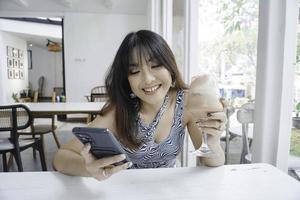 una mujer asiática feliz sonriendo en un restaurante, usando una camiseta sin mangas y sosteniendo su teléfono foto