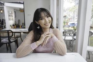 A smiling Asian woman wearing pink dress while sitting near window photo