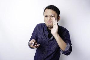 The angry and mad face of Asian man in blue shirt holding his phone isolated white background. photo