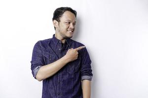 Excited Asian man wearing blue shirt pointing at the copy space beside him, isolated by white background photo