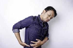 Tired upset young man wears blue shirt suffering from pain, muscle spasm at workplace. Fatigue, deadline, pain and incorrect posture photo