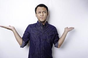 A portrait of an Asian man wearing a blue shirt looks so confused between choices, isolated by a white background photo