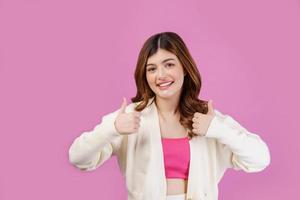 Portrait of Young happy cheerful woman showing thumb up and looking at camera isolated over pink background photo