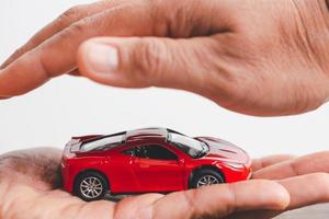 manos femeninas y coche como protección del concepto de coche. mujer agente de seguros que cubre coche de juguete sobre fondo blanco, primer plano. protección de las manos del coche sobre la mesa de madera. seguros de autos y negocio automotriz foto