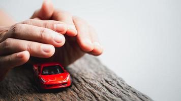 Female hands and car as protection of car concept. Woman insurance agent covering toy car on white background, closeup. Hands protecting of car over wooden table. Car insurance and automotive business photo