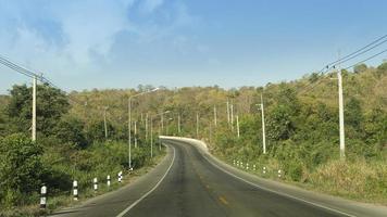 Traffic route of asphalt road that goes straight up the mountain and curvy path. On both sides of the road there are electric poles lined up. Background of mountain under the blue sky. photo