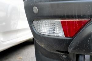 Back of a car that is soiled with dust. On back of car with white and red rear lights for reversing lights. And blurred of other car on the side. photo