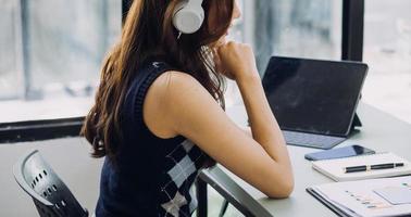 Young business woman sitting in office at table and using smartphone. On desk is laptop and tablet computer, on screen charts and graphs. Woman analyzing data. Student learning online. photo