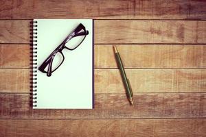 Blank notebook with pen and glasses on wood background photo