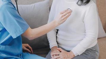 Homecare nursing service and elderly people cardiology healthcare. Close up of young hispanic female doctor nurse check mature caucasian man patient heartbeat using stethoscope during visit video