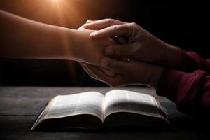 Hands folded in prayer on a Holy Bible in church concept for faith, spirituality and religion, man praying in morning. Man hand with Bible praying. Person Christian who faith in Jesus worship in dark.