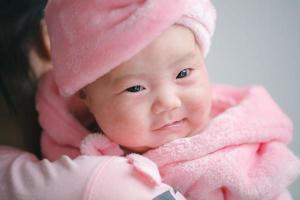 Closeup cute child care with mother indoor. Happy little toddler baby girl smiling lying on bed on white sheet at home looking at camera. Copy space for text. Infancy, healthcare and babyhood concept. photo