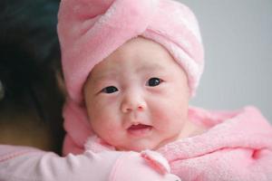 Closeup cute child care with mother indoor. Happy little toddler baby girl smiling lying on bed on white sheet at home looking at camera. Copy space for text. Infancy, healthcare and babyhood concept. photo