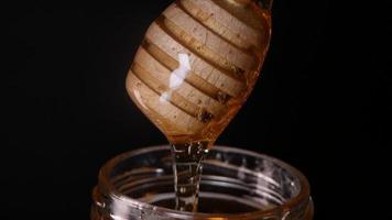 mel fluindo de uma colher de mel de madeira em um fundo preto video