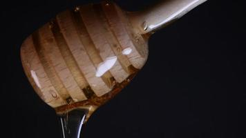 Flowing honey from a wooden honey spoon on a black background video