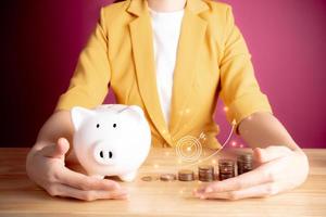 Businesswoman with rows of coins, archery target, arrow going up for account finance bank business concept. coins with piggy bank. Save money for prepare in the future. pink background. photo
