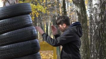 A boy boxing training on the park punching a punch bag hanging from a tree. video