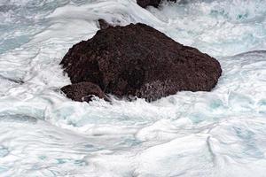 sea in tempest breaking waves on lava rock cliff photo