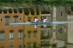 florencia, italia - 1 de septiembre de 2018 - gente remando en el río de la ciudad con reflejo de casas antiguas foto