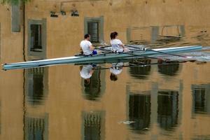 florencia, italia - 1 de septiembre de 2018 - gente remando en el río de la ciudad con reflejo de casas antiguas foto