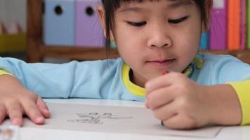 joyeuse petite fille heureuse dessinant avec des crayons sur papier assis à table dans sa chambre à la maison. créativité et développement de la motricité fine. video