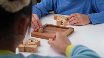 weinig broers en zussen spelen houten bord spel boter kaas en eieren Aan tafel in leven kamer. familie uitgeven tijd samen Aan weekend. video