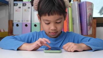 menina bonitinha segurando smartphone olhando para a tela sorrindo usando o aplicativo, jogando jogos online, assistindo desenhos animados na sala de estar em casa. crianças e conceito de tecnologia moderna video