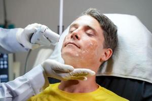 hombre guapo de primer plano que tiene terapia de luz de color para estimular la piel facial por el bienestar de un cosmetólogo profesional. foto