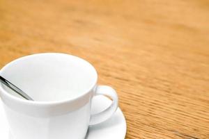 Closeup and crop white coffee cup and spoon with saucer on wooden table. photo