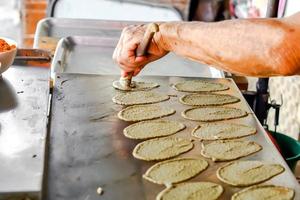 la mano del anciano está haciendo dulces panqueques crujientes tailandeses para los clientes. en la foto pone postre de hilos dorados encima de crema dulce y láminas de masa.