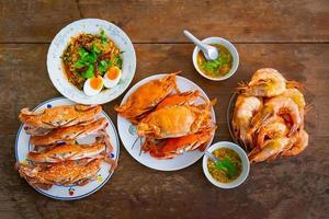 Top view Boiled Crabs and Shrimps in the white ceramic and glass dish on the vintage wooden table. photo