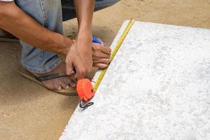 Worker is measure brick foam plate board before installation on construction site by tapeline.
