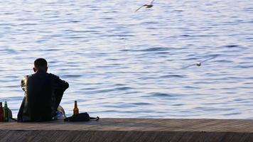 hombre sentado en la playa mirando las gaviotas voladoras