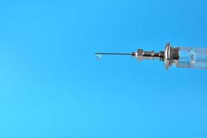 syringe with a drop of medication at the end of the needle on a blue background. photo