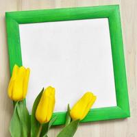 maqueta de marco verde brillante y tres tulipanes amarillos sobre fondo de madera foto