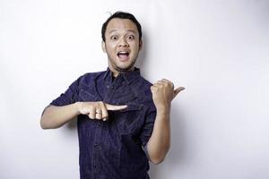 Shocked Asian man wearing blue shirt pointing at the copy space beside him, isolated by white background photo