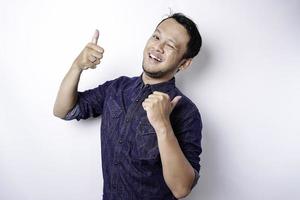 Excited Asian man wearing blue shirt pointing at the copy space beside him, isolated by white background photo