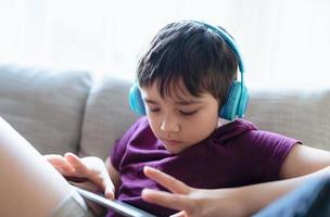 Education concept,High key portrait primary school Kid reading E-book on tablet for homework,Child wearing headphone playing game online on internet,boy sitting on sofa watching cartoon on digital pad photo