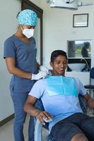 mujer dentista en el consultorio dental hablando con un paciente joven y preparándose para el tratamiento.