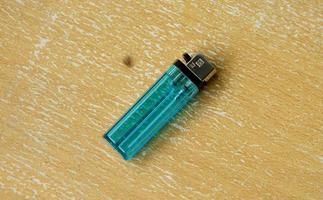 Jakarta, Indonesia - January 27th, 2023 - Blue cyan classic indonesian lighter with SNI standard logo. Korek api. Object to light fire or cigarettes isolated on wooden surface background. photo