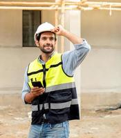 arquitecto o ingeniero masculino que usa teléfono móvil para comunicarse mientras trabaja en el sitio de construcción. el contratista de construcción profesional que se encuentra en el sitio de desarrollo de viviendas usa un teléfono inteligente en el trabajo. foto
