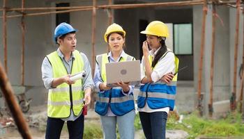 Female construction engineer holds computer laptop meeting with architect teamwork. Multiracial people group wear safety hardhat using laptop brainstorming on housing development at construction site photo