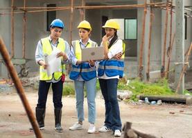 Female construction engineer holds computer laptop meeting with architect teamwork. Multiracial people group wear safety hardhat using laptop brainstorming on housing development at construction site photo