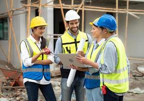 Female construction engineer holds computer laptop meeting with architect teamwork. Multiracial people group wear safety hardhat using laptop brainstorming on housing development at construction site photo