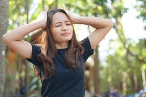 mujer asiática pensando mucho causando dolor de cabeza fondo de bosque verde foto