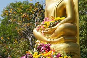 The golden Buddha image has many people bringing flowers to worship. photo