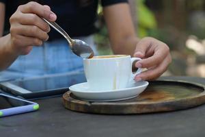 café caliente en manos humanas. flores de espuma de café en una taza blanca. fondo de madera gris foto