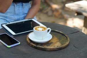 café caliente en manos humanas. flores de espuma de café en una taza blanca. fondo de madera gris foto