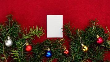 Piece of paper for Christmas wishes on a red background with branches of Christmas tree and Christmas balls. photo