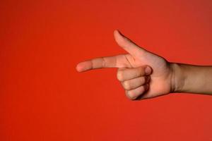 mano humana con dedos doblados, muestra un dedo índice que simboliza una pistola, aislado en un fondo rojo foto